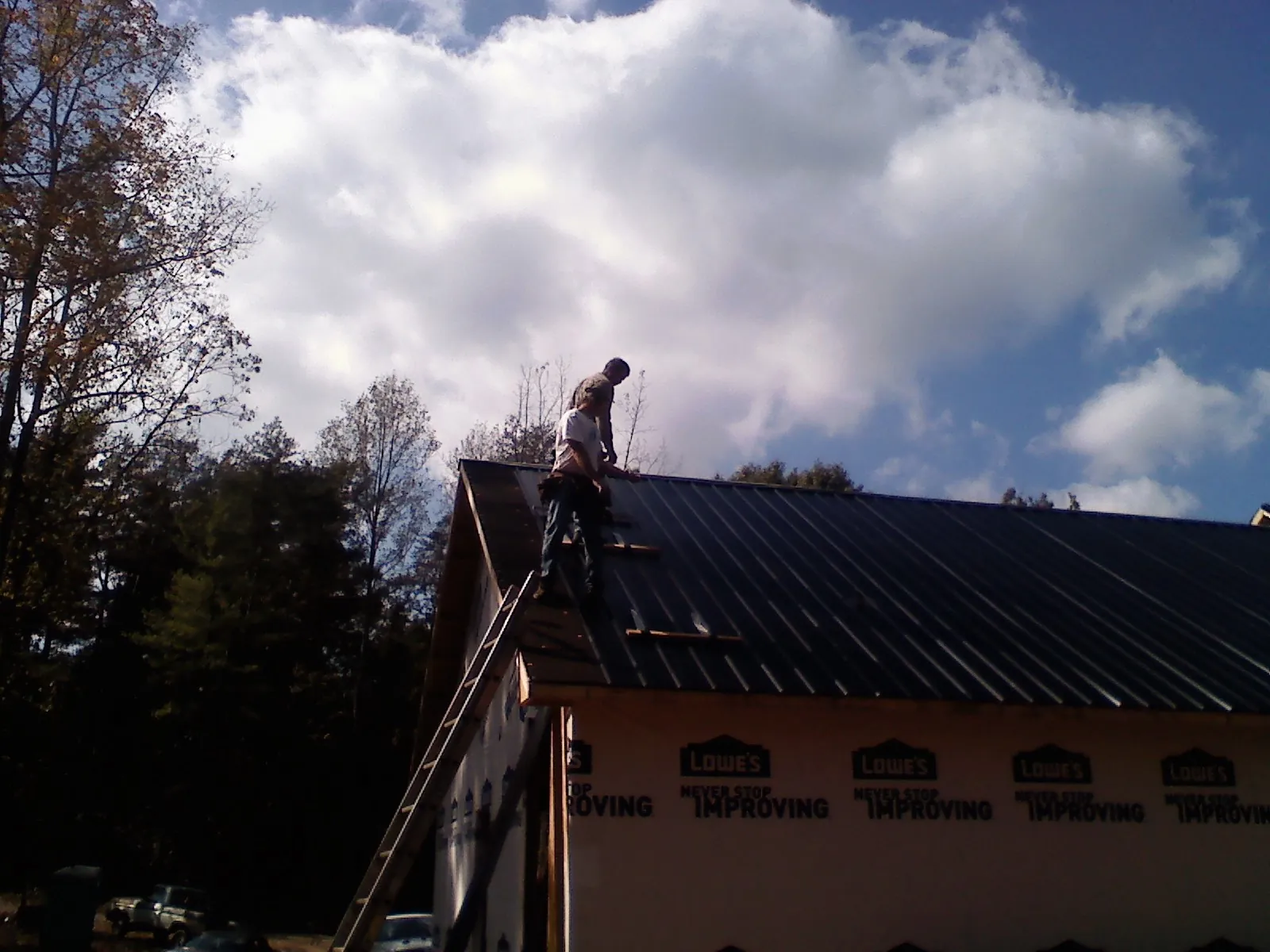 Roofer fastening dark metal panels high against a cloudy sky, from a Roof Inspection job in Collinsville