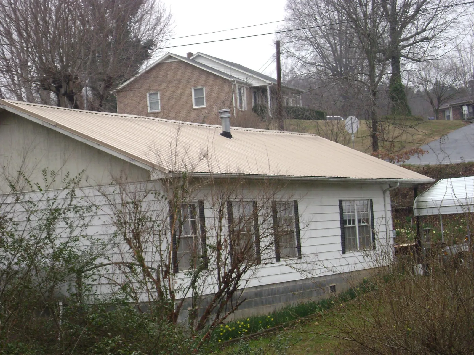 Tan metal roof on a white sided house set into a hillside — Commercial Roofing by Roofing Brothers in Collinsville